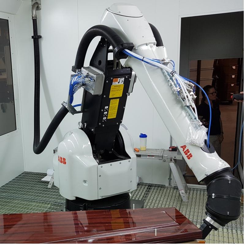 ABB paint robot with spray gun inside a Mexx-built paint booth, finishing a glossy timber panel